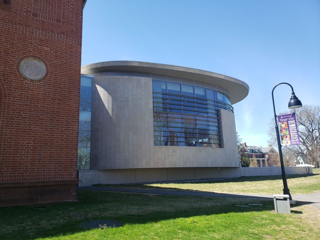 Back end of the Smith College Neilson Library, a modern-style round concrete building with glass windows in the middle, and a connector to the brick half of the library.
